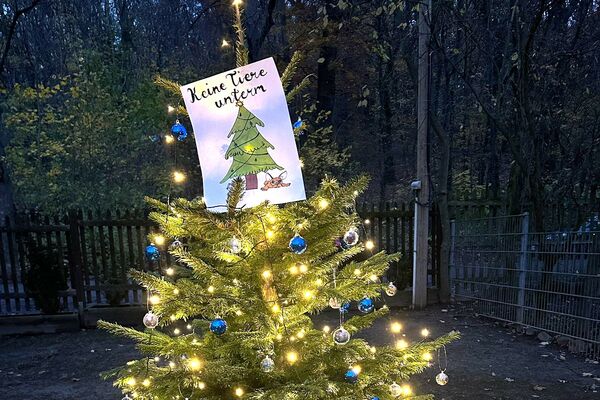 Ein beleuchteter Weihnachtsbaum mit Plakat oben "Keine Tiere unterm Weihnachtsbaum"