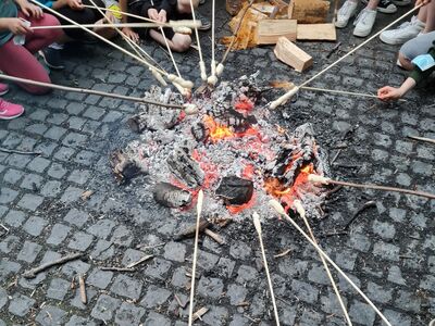 Mehrere Stöcke mit Brot werden in ein Lagerfeuer gehalten.