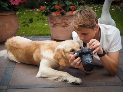 Ein Junge liegt neben einem hellbraunen Hund auf einem Terrassenboden und läßt den Hund in durch die Kamera schauen.