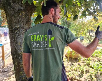 Rückenansicht eines Mannes mit "Daumen hoch"-Zeichen. Auf dem T-Shirt des Mannes stehen die Unternehmensdaten von Grays Garden.
