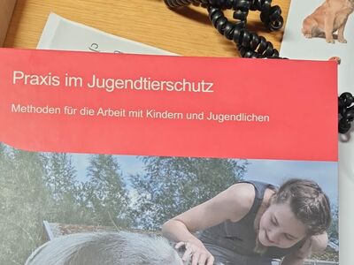 Das Deckblatt eine Ordners "Praxis im Jugendtierschutz" mit dem Logo des Deutschen Tierschutzbundes und dem Foto eines Mädchens, dass draußen ein Schwein streichelt.