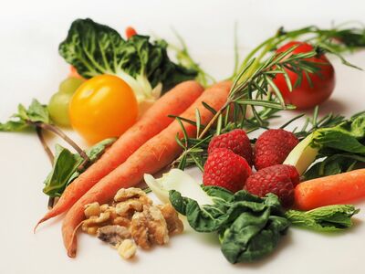 Möhren, Tomaten, Trauben und anderes Obst und Gemüse sowie Kräuter und Walnüsse auf einer weißen Fläche leigend.