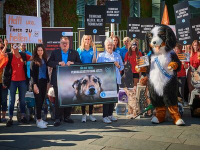 Eine Personengruppe mit Plakaten und eine Person im Hundekostüm fordern mehr Unterstützung für Tierheime.