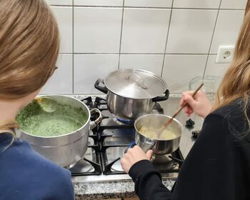 Zwei Mädchen beim Kochen am Gasherd.