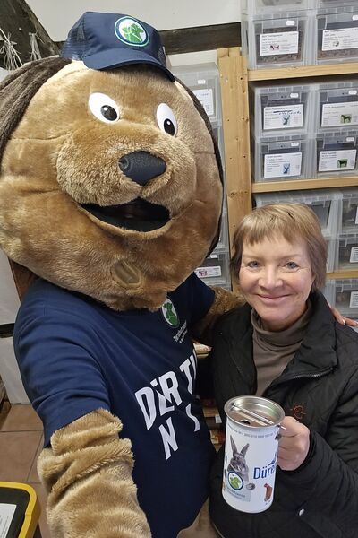 Ein großer Plüschhund hält eine Eine Frau mit Spendendose im Arm.